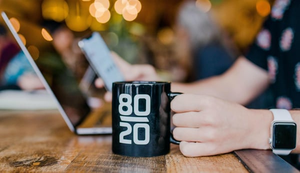 Image shows someone at a laptop with a coffee mug that says 80 over 20