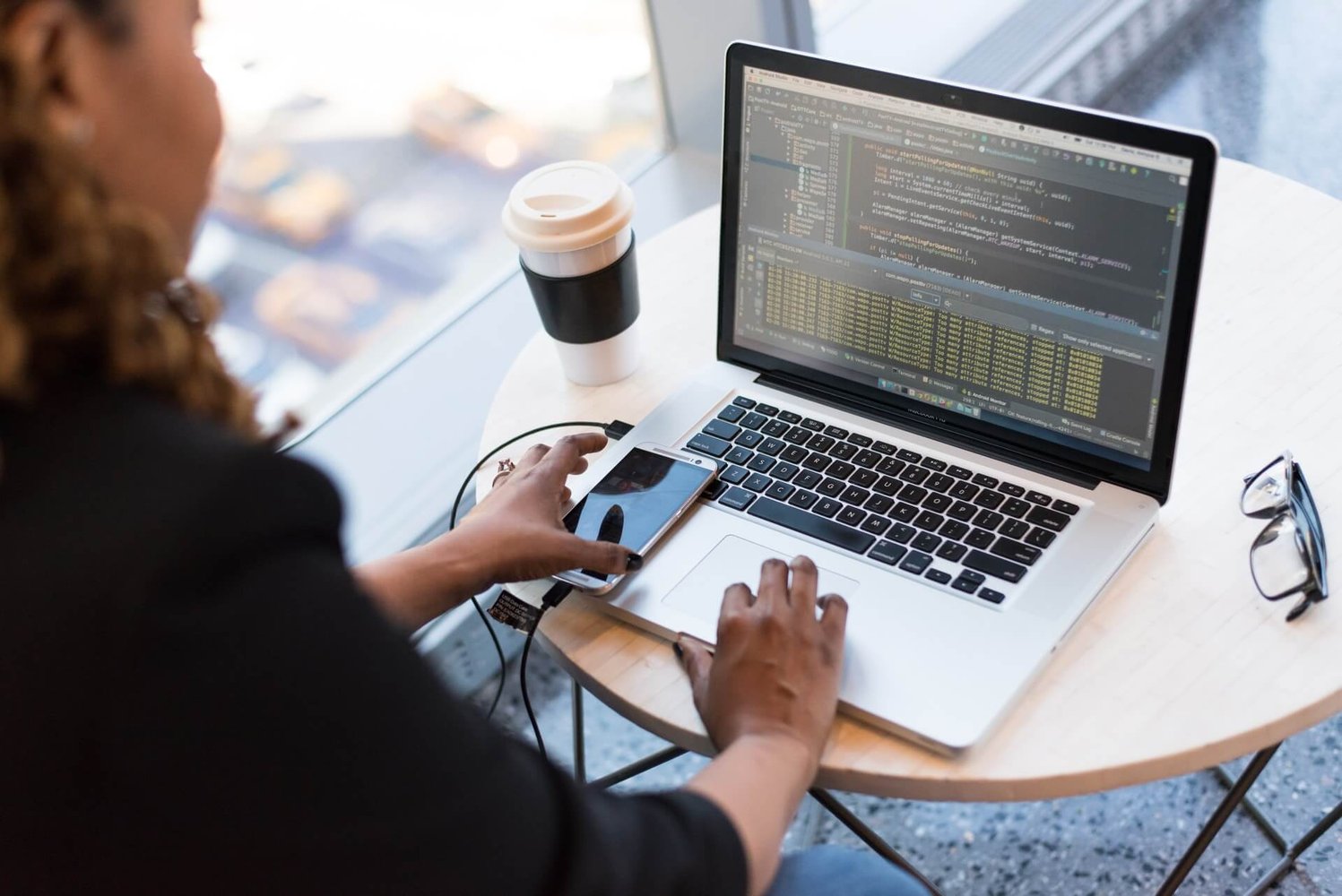 Image shows a woman sitting at a laptop with lines of code attached and her phone on the laptop