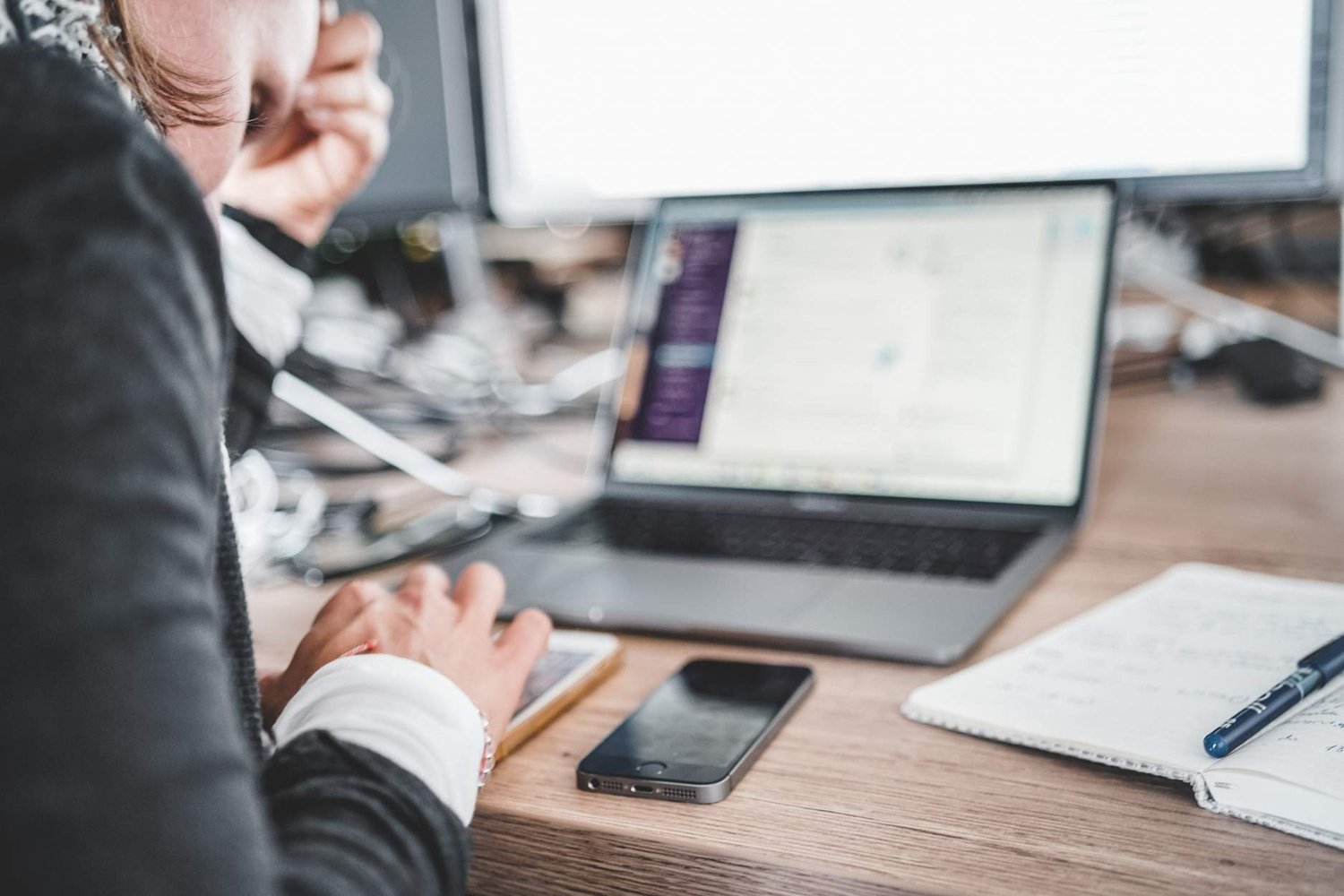 Person looking at phone and laptop on their desk