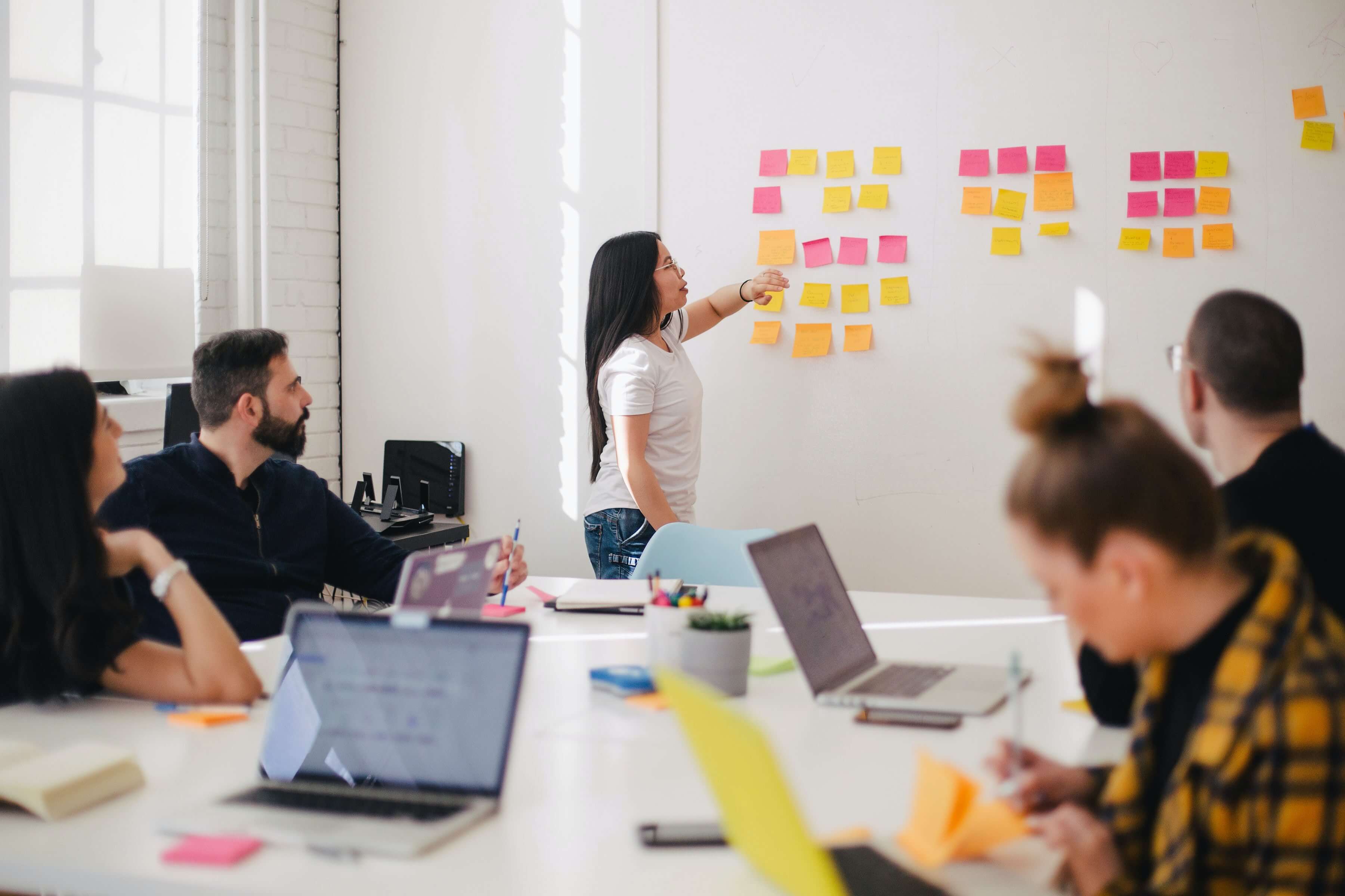 woman standing at whiteboard presenting to a group (image for blog post The QA benefits of an Agile automated testing strategy)